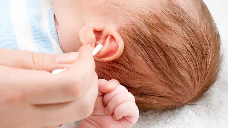 A close-up of a mother using cotton swabs to clean earwax from her baby's ears. Concept of infant and newborn hygiene and healthcare. Caring parents with young children.