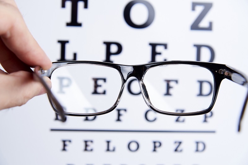 Prescription glasses in hands against the background of an eye chart